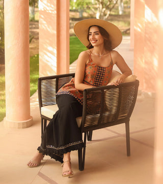 Woman sitting on a wicker chair wearing a sun hat in a sunlit outdoor setting.
